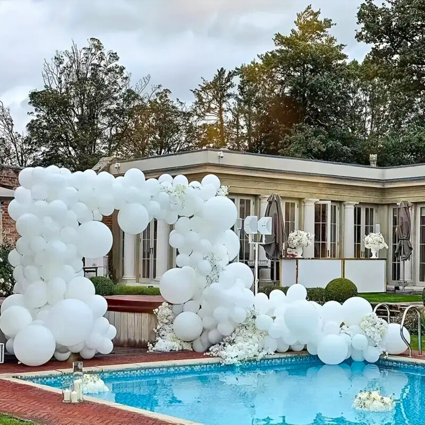 Luxurious outdoor balloon arch setup using matte white balloons in varying sizes, styled beside a pool at a modern venue, ideal for baby showers, gender reveals, or weddings.
